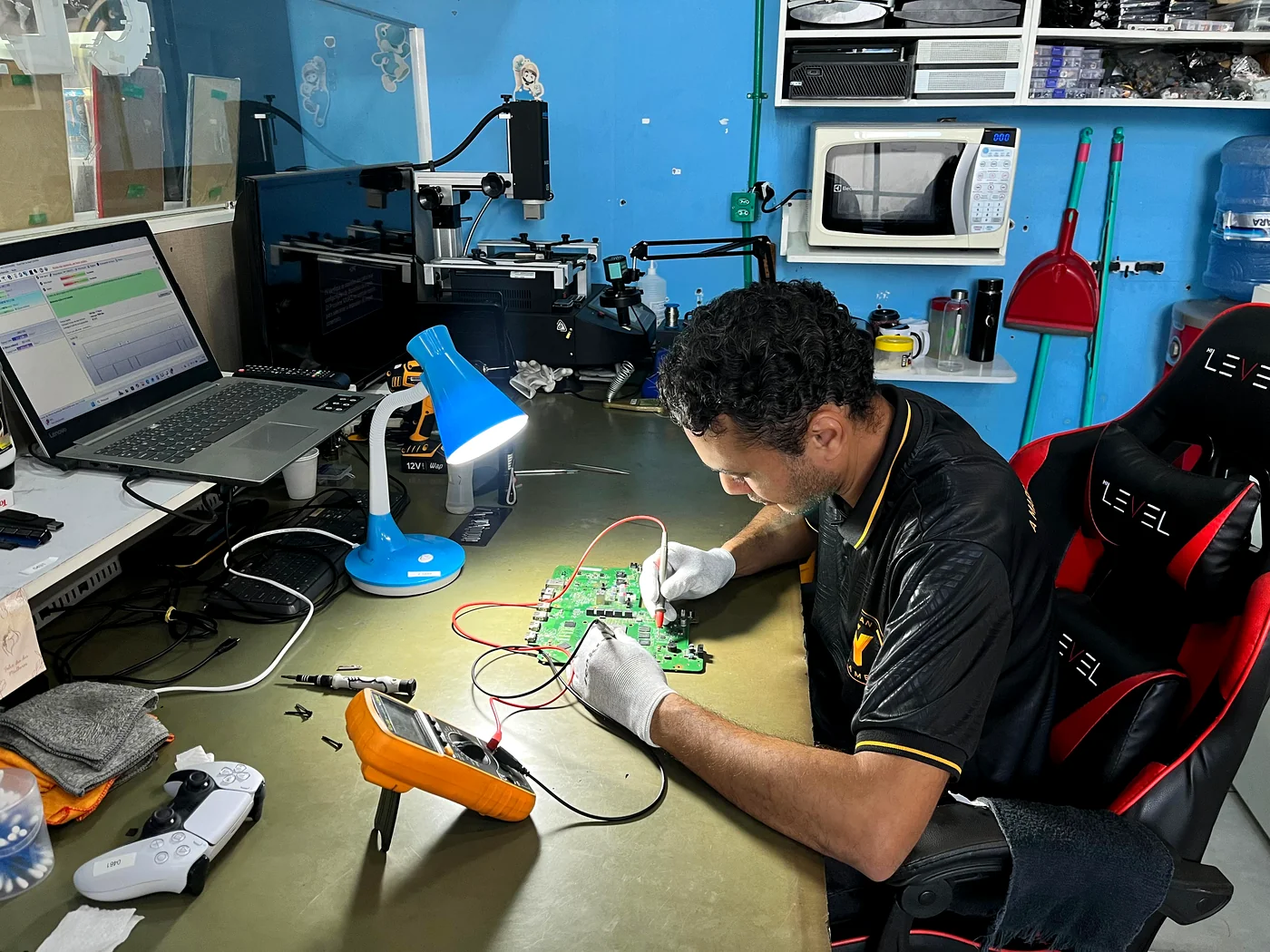 Profissional da CLAN Y GAMER concentrado em reparo de equipamento eletrônico na bancada.