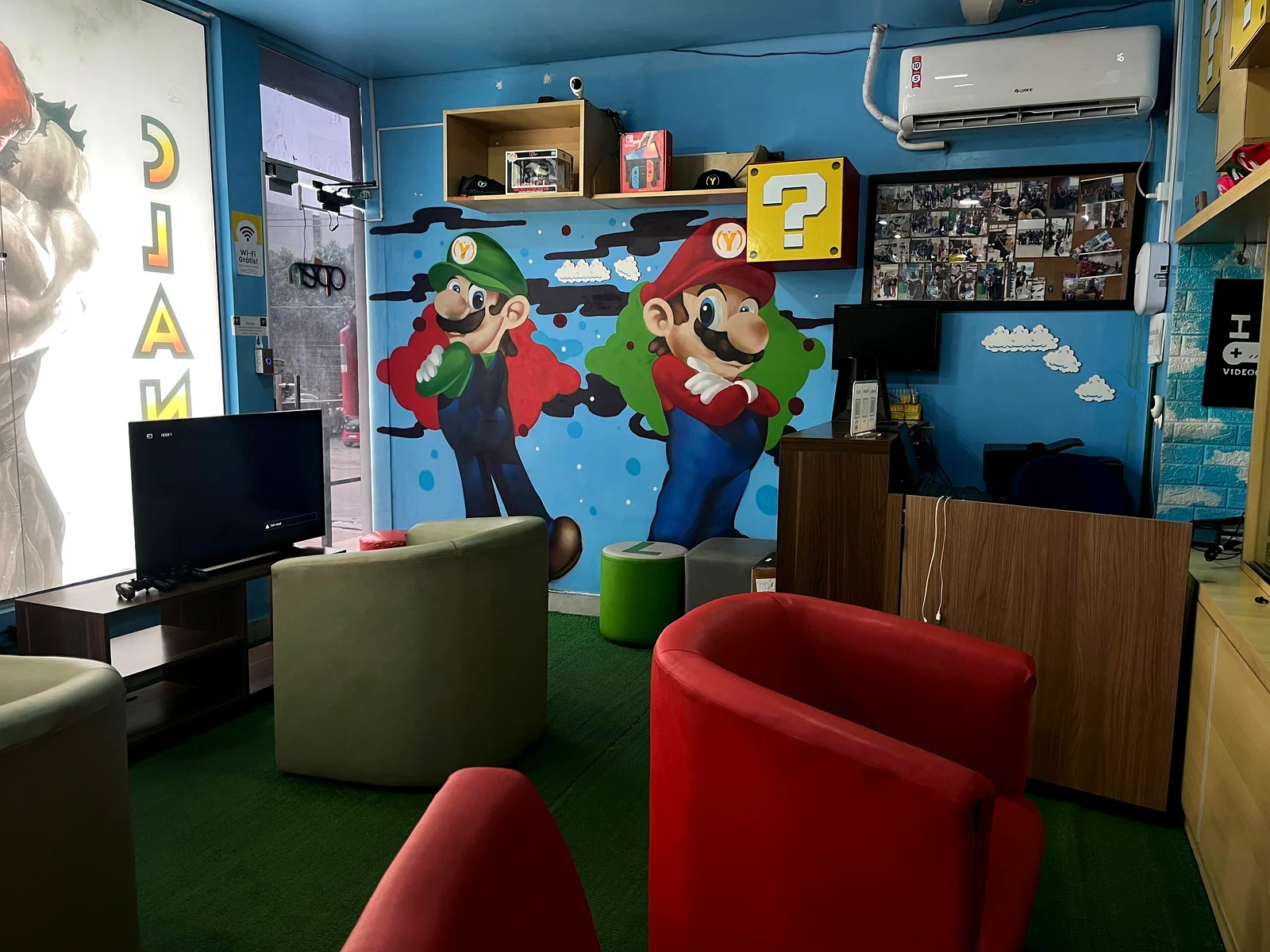 Vista panorâmica do interior da loja CLAN Y GAMER em Adrianópolis com decoração temática gamer, sofás e vitrines de produtos.