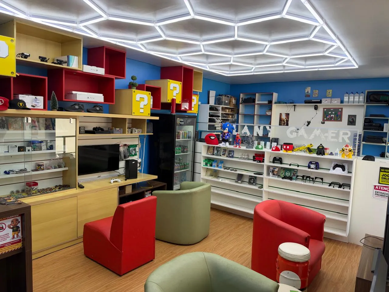 Interior da matriz CLAN Y GAMER em Adrianópolis, Manaus, com poltronas vermelhas e verdes, vitrines e iluminação geométrica no teto.